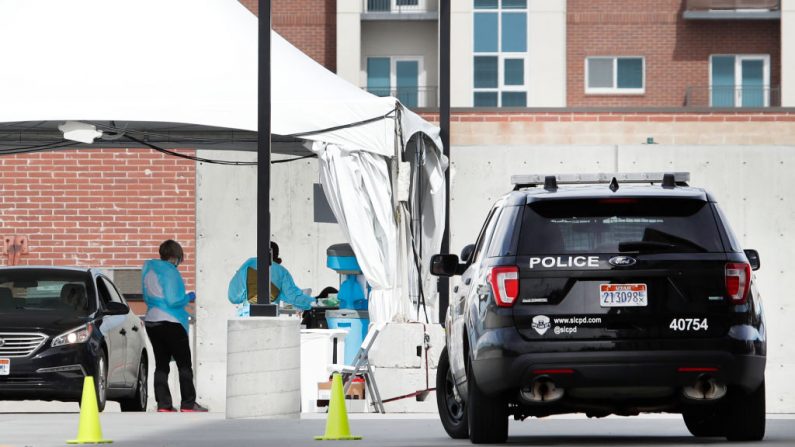 Un coche de policía está aparcado cerca como trabajadores en equipo de protección, procesan a un paciente en un coche en una de las primeras instalaciones de prueba para el virus del Coronavirus (COVID-19) en un aparcamiento fuera de la Clínica de Salud Sugar House de la Universidad de Utah en Salt Lake City, Utah el 16 de marzo de 2020. (Foto de GEORGE FREY / AFP vía Getty Images)
