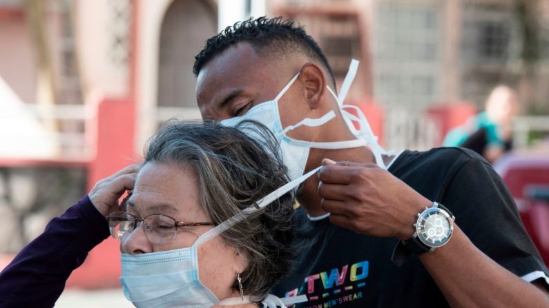 Un hombre le pone una mascarilla a una mujer como medida preventiva contra la propagación del virus del PCCh, en San José, el 16 de marzo de 2020. (Foto de EZEQUIEL BECERRA/AFP vía Getty Images)
