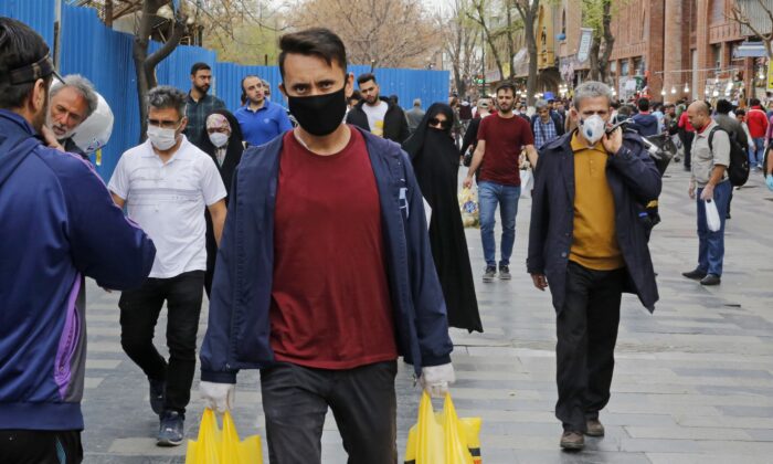 Iraníes, algunos con máscaras protectoras, caminan fuera del gran bazar de la capital Teherán, durante la crisis de la pandemia del virus del PCCh, el 18 de marzo de 2020. (-/AFP a través de Getty Images)