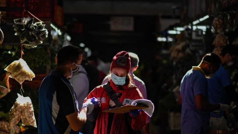 Una mujer con una máscara facial como medida preventiva contra la propagación del virus del PCCh, anota las cosas mientras hace sus compras en un mercado municipal de Caracas, Venezuela, el 20 de marzo de 2020. (FEDERICO PARRA/AFP vía Getty Images)