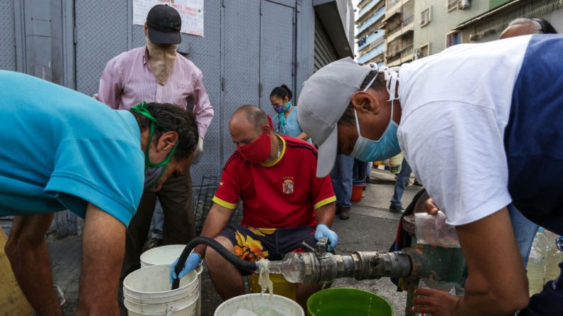 Gente usando máscaras faciales como medida preventiva contra la pandemia global del virus del PCCh mientras recogen agua de una tubería de la calle en Caracas, el 21 de marzo de 2020. (Cristian Hernandez/AFP vía Getty Images)