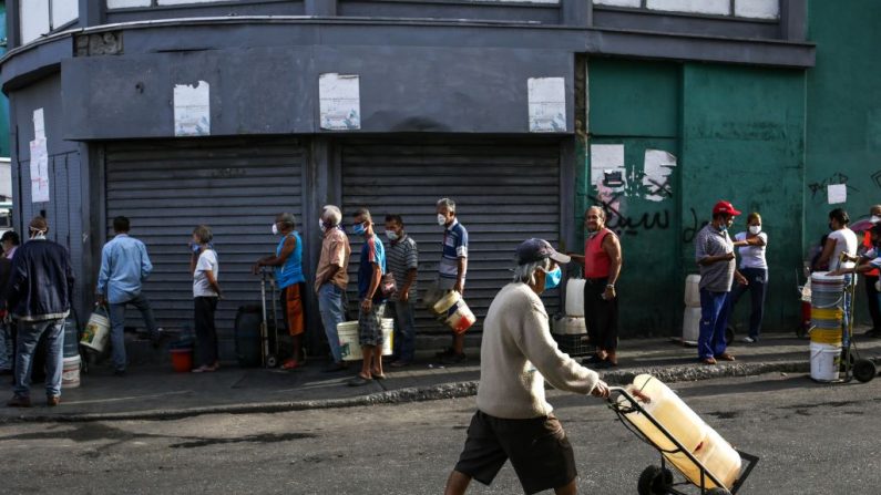 La gente usa máscaras faciales como medida preventiva contra la pandemia global del virus del PCCh mientras hacen cola para recoger agua de una tubería de la calle en Caracas, Venezuela, el 21 de marzo de 2020. (CRISTIAN HERNANDEZ/AFP vía Getty Images)