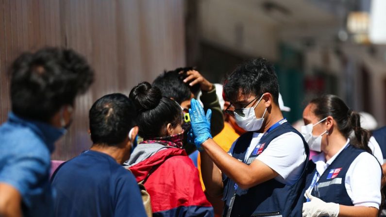 Trabajadores sanitarios chilenos comprueban la temperatura de los peruanos que hacen cola para un salvoconducto fuera de su consulado en la ciudad chilena de Arica, en la frontera con Perú, el 23 de marzo de 2020. (PATRICIO BANDA/AFP vía Getty Images)