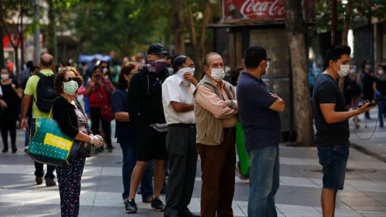 Personas con máscaras faciales hacen cola en el cajero automático de un banco durante la pandemia del virus del PCCh el 24 de marzo de 2020 en Santiago de Chile. (Marcelo Hernandez/Getty Images)