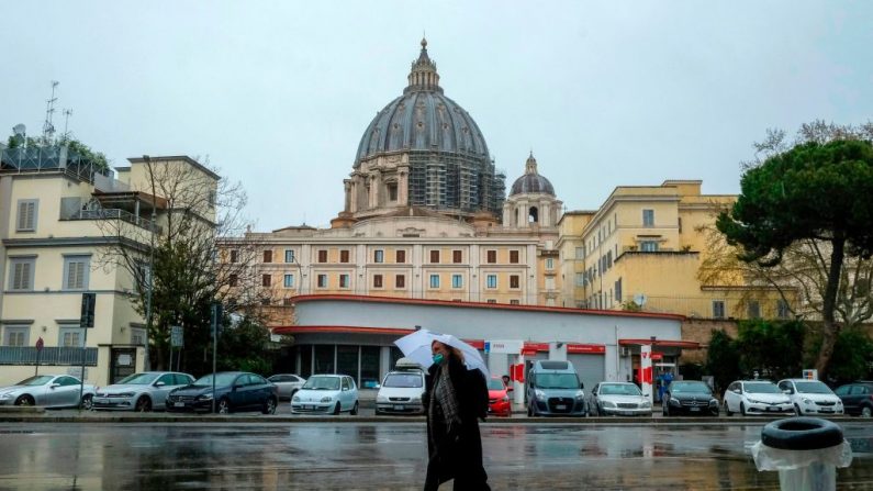 Una mujer con una máscara facial camina por una calle pasando la residencia de Santa Marta en el Vaticano (parte posterior c) en Roma, el 26 de marzo de 2020 durante el cierre del país después de la nueva pandemia del virus del PCCh. (ANDREAS SOLARO/AFP vía Getty Images)