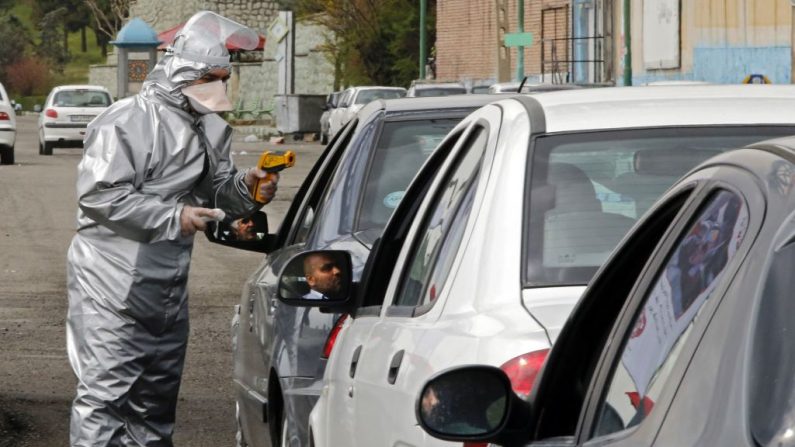 Miembros de la Media Luna Roja iraní realizan pruebas a personas para detectar los síntomas del virus del PCCh, mientras la policía bloqueaba la autopista de Teherán a Alborz para comprobar todos los coches siguiendo las órdenes del gobierno, en las afueras de Teherán, Irán, el 26 de marzo de 2020. (STR/AFP vía Getty Images)