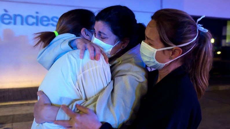 Trabajadoras sanitarias que se enfrentan a la nueva crisis del virus del PCCh en España, se abrazan entre sí mientras son vitoreadas por la gente fuera del hospital La Fe de Valencia el 26 de marzo de 2020. (Foto de JOSE JORDANIA/AFP vía Getty Images)