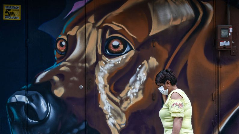 Una mujer con una máscara facial como medida preventiva contra la propagación del virus del PCCh, pasa por delante de un mural en Bogotá, Colombia, el 28 de marzo de 2020. (JUAN BARRETO/AFP vía Getty Images)