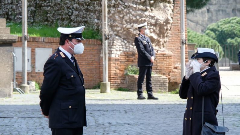 Oficiales de la policía municipal con una máscara facial se pararon frente al ayuntamiento de Roma en Capitoline Hill (Campidoglio) mientras se enarbolan banderas a media asta en ciudades de Italia para conmemorar a las víctimas del virus del PCCh, el 31 de marzo de 2020. (ANDREAS SOLARO / AFP a través de Getty Images)