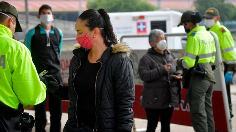 Miembros de la policía colombiana, usando máscaras faciales como medida preventiva contra la propagación del virus del PCCh, revisan la identificación de las personas a la entrada de una estación de autobuses, en Soacha, cerca de Bogotá, Colombia, el 31 de marzo de 2020. (Raúl ARBOLEDA/AFP vía Getty Images)