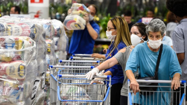 Personas con máscaras protectoras hacen cola para recibir paquetes de alimentos en un mercado local el 31 de marzo de 2020 en Belo Horizonte, Brasil. El ayuntamiento de Belo Horizonte comenzó a distribuir paquetes de alimentos a las familias de los estudiantes matriculados en las escuelas municipales. La iniciativa se desarrolló para reemplazar las comidas escolares, ya que las clases se suspenden debido al virus del PCCh. La distribución durará mientras se suspendan las clases, y cada familia recibirá un paquete por mes. (Pedro Vilela/Getty Images)