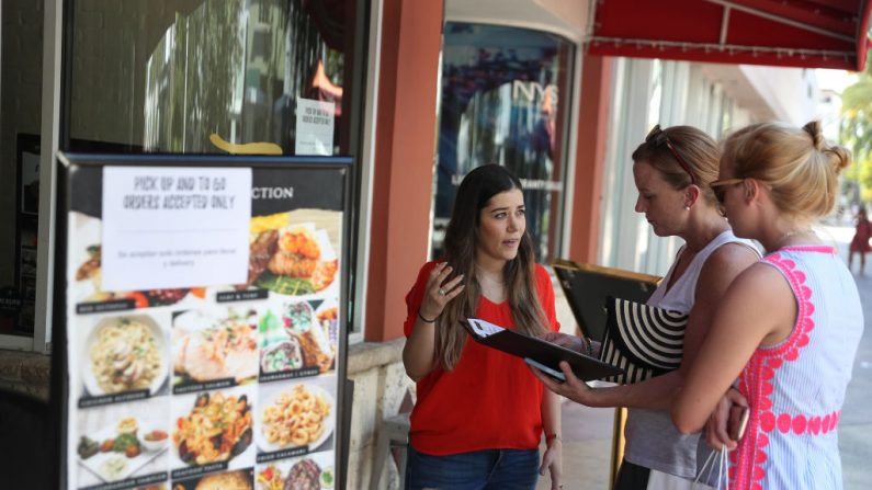 Rima Bou repasa el menú de comida para llevar con Lisa Ellegard y su hija, Madeleine Ellegard, en el restaurante 7 Spices del centro comercial Lincoln Road mientras la ciudad ordena a los propietarios de los restaurantes que cierren en un intento de detener la propagación del virus del PCCh el 18 de marzo de 2020 en Miami Beach, Florida, EE.UU. (Joe Raedle/Getty Images)