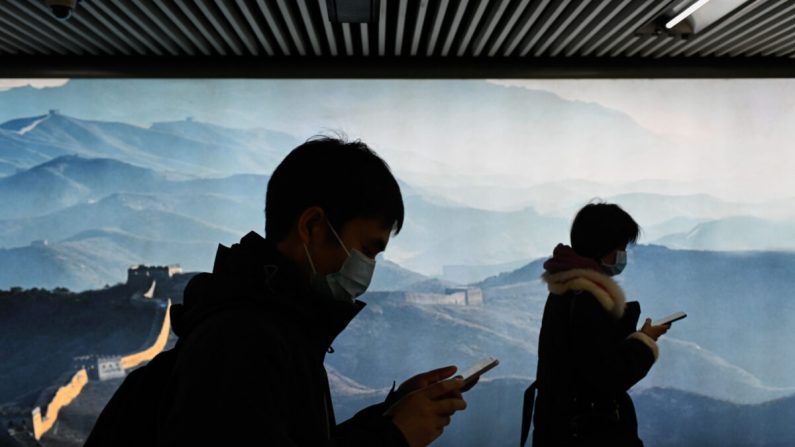 Un hombre y una mujer con máscaras usan su teléfono móvil mientras caminan en una estación de metro en Beijing el 11 de marzo de 2020. (Wang Zhao/AFP a través de Getty Images)