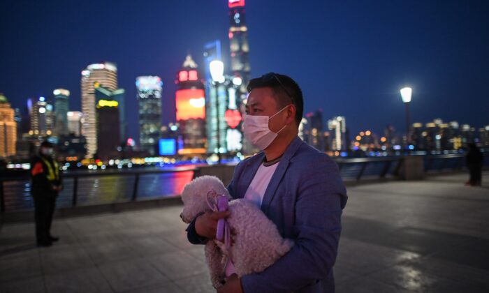 Un hombre con una máscara facial, en medio de las preocupaciones por el brote del virus del PCCh, camina con su perro por el paseo marítimo del Bund a lo largo del río Huangpu en Shanghai, China, el 20 de marzo de 2020. (Héctor Retamal/AFP a través de Getty Images)
