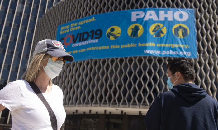 La gente usa máscaras cuando pasa por delante de un cartel de concienciación sobre el virus del PCCh afuera de la Organización Mundial de la Salud en Washington el 30 de marzo de 2020. (Andrew Caballero-Reynolds/AFP a través de Getty Images)