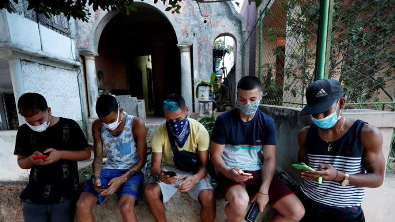 Un grupo de jóvenes con tapabocas fue registrado al mirar sus teléfonos celulares en un barrio de La Habana (Cuba). EFE/Yander Zamora