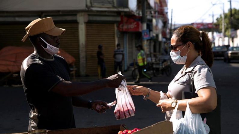SANTO DOMINGO, (REPÚBLICA DOMINICANA) 28/03/2020.- Un haitiano vende cerezas a una mujer, cuando las calles se encuentran casi vacías desde la entrada en vigor del estado de emergencia. EFE/ Orlando Barría
