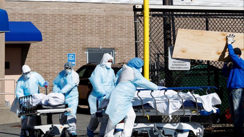 Trabajadores de la salud transportan dos cuerpos más allá de un obrero de la construcción construyendo los interiores de una de las dos morgues temporales establecidas fuera del Centro Médico Wyckoff Heights para atender al gran número de víctimas de la enfermedad COVID-19 en Brooklyn, Nueva York, EE.UU., el 06 de abril de 2020. EFE/EPA/JUSTIN LANE