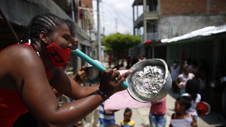 Una mujer golpea una cacerola en el barrio Tercer Milenio este jueves en Cali (Colombia). Decenas de personas salieron de sus casas haciendo sonar cacerolas para reclamar a la alcaldía por la falta de ayudas y alimentos en medio de la cuarentena por la emergencia del Covid-19. EFE/ Ernesto Guzmán Jr
