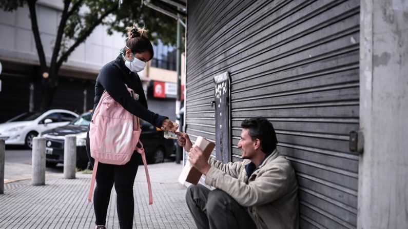 BUENOS AIRES (ARGENTINA), 03/04/2020.- Una mujer da dinero a un hombre sin hogar cerca a un banco donde pagan jubilaciones y planes sociales este viernes, en Buenos Aires (Argentina).  EFE/Juan Ignacio Roncoroni
