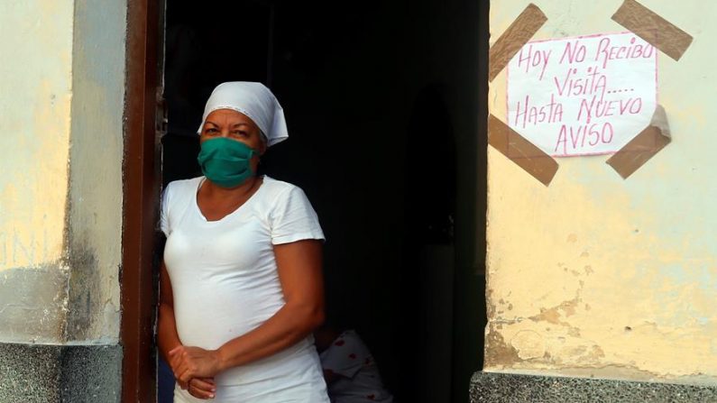 Una mujer posa para una foto a la entrada de su casa junto a un cartel de prohibición de visitas hasta nuevo aviso el 16 de abril de 2020, en La Habana (Cuba). EFE/Ernesto Mastrascusa