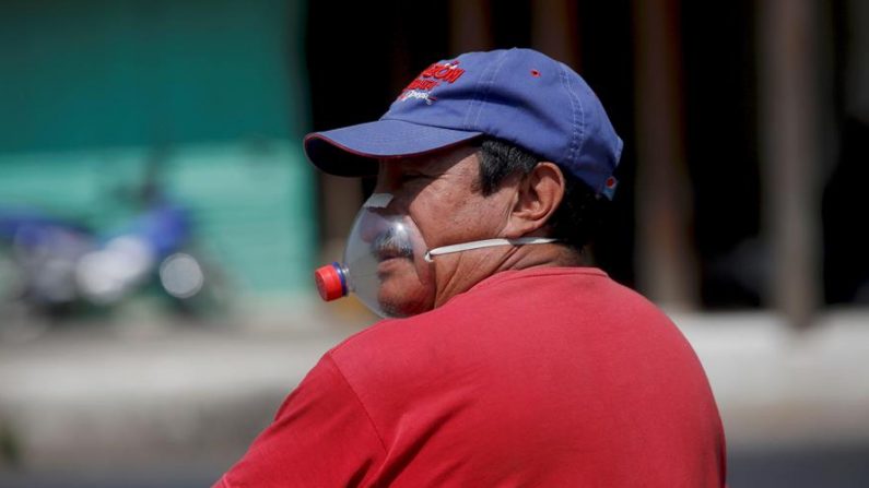 Un hombre con una mascarilla improvisada con una envase de gaseosa pasa frente a la fachada de la iglesia San Felipe, el 10 de abril de 2020 en la Antigua Guatemala (Guatemala). EFE/Esteban Biba