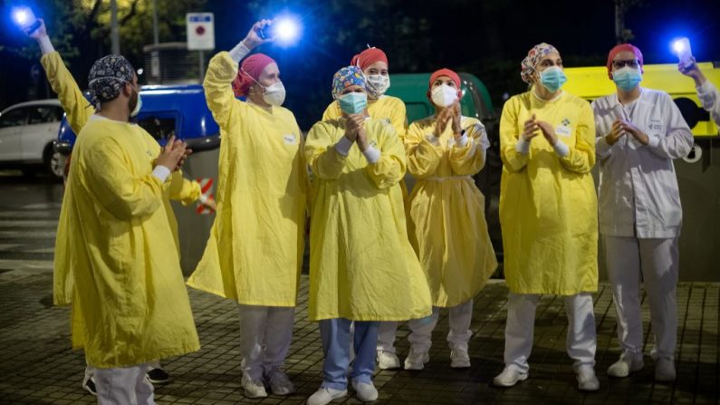 Los trabajadores de la salud que llevan máscaras faciales y trajes protectores reconocen los aplausos fuera del Hospital de Barcelona a las personas en sus casas el 13 de abril de 2020 en Barcelona (España). (Foto de JOSEP LAGO/AFP vía Getty Images)