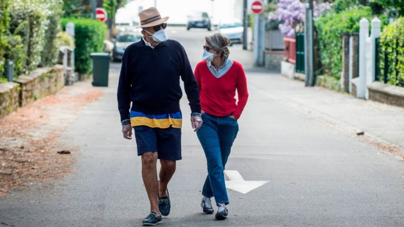 Una pareja camina con máscara protectora por una calle vacía en La Baule, oeste de Francia, el 13 de abril de 2020, durante un estricto bloqueo en toda Francia para detener la propagación del virus del PCCh. (SEBASTIEN SALOM-GOMIS/AFP vía Getty Images)