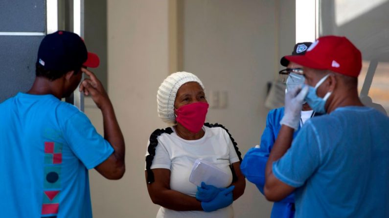 Una mujer con guantes y máscara facial como medida preventiva contra la propagación del virus del PCCh habla con los hombres a la entrada de la sala de emergencias del Hospital Moscoso Puello en Santo Domingo, República Dominicana, el 17 de abril de 2020. (ERIKA SANTELICES/afp/AFP vía Getty Images)