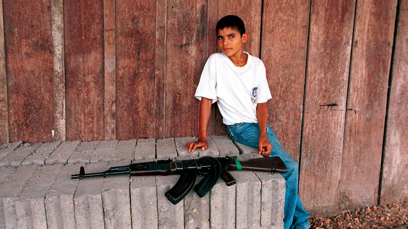 Un niño sentado cerca de un rifle de asalto AK-47 en un puesto de control de las FARC el 26 de febrero de 2001 en Cristales, Colombia. (Foto de Carlos Villalón/Newsmakers)