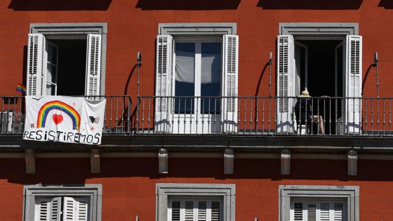 Una mujer se sienta en su balcón cerca de una pancarta que dice "Resistiremos" en Madrid, España, el 3 de abril de 2020 durante un cierre nacional para prevenir la propagación del virus del PCCh. (GABRIEL BOUYS/AFP vía Getty Images)