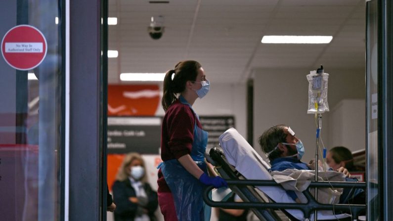 Un profesional médico en EPP, que lleva guantes, un delantal y una mascarilla facial como medida de precaución contra el virus del PCCh, empuja a un paciente, también con una mascarilla facial, mientras está acostado en una cama, dentro del Hospital de Santo Tomás en el norte de Londres, Inglaterra, el 1 de abril de 2020. (DANIEL LEAL-OLIVAS/AFP vía Getty Images)