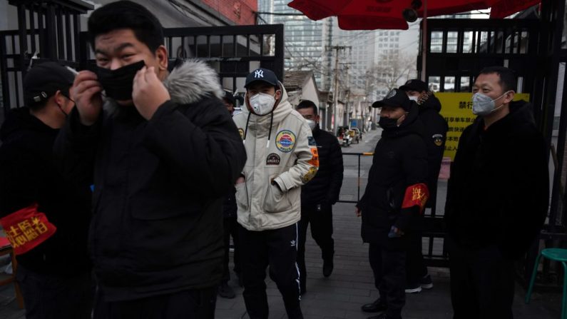 Los residentes llevan mascarillas cuando pasan por delante de los voluntarios que están en un puesto de control a la entrada de un callejón en Beijing el 21 de febrero de 2020. (Greg Baker/AFP vía Getty Images)
