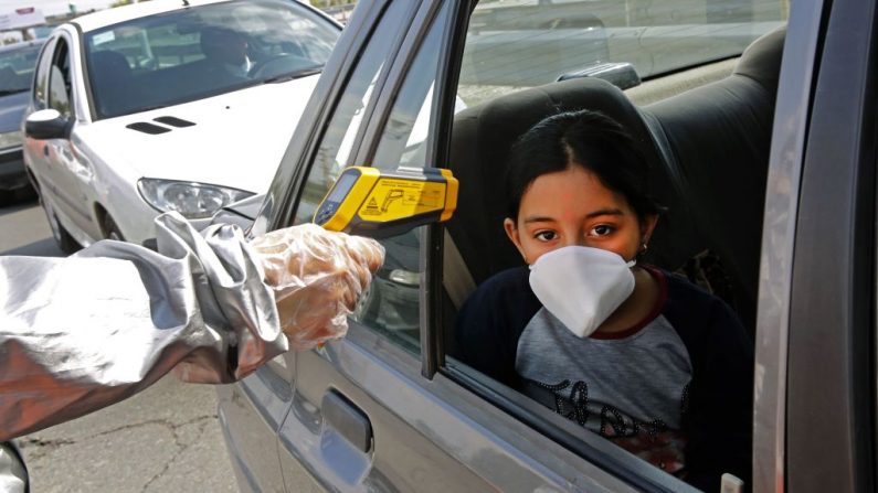 Miembros de la Media Luna Roja iraní realizan pruebas a personas para detectar los síntomas del virus del PCCh, mientras la policía bloqueaba la autopista de Teherán a Alborz para comprobar todos los coches siguiendo las órdenes del gobierno iraní, en las afueras de Teherán, Irán, el 26 de marzo de 2020. (STR/AFP vía Getty Images)