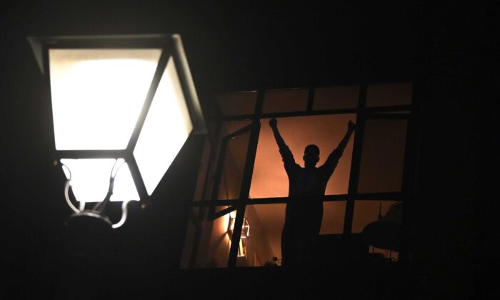 Una persona confinada en su casa hace gestos y aplaude desde una ventana para rendir homenaje a los trabajadores sanitarios que se ocupan de la enfermedad COVID-19 durante un encierro nacional para evitar la propagación de la nueva pandemia de virus del PCCh en Madrid, España, el 28 de marzo de 2020. (Gabriel Bouys/AFP vía Getty Images)