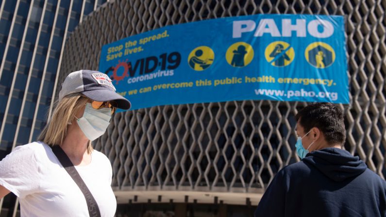 Personas con máscaras pasan por delante de un cartel de concienciación sobre el coronavirus en las afueras de la Organización Mundial de la Salud en Washington, DC, el 30 de marzo de 2020. (ANDREW CABALLERO-REYNOLDS/AFP vía Getty Images)