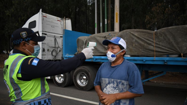 Un policía de tránsito controla la temperatura de un camionero como medida preventiva contra el virus del PCCh, durante un toque de queda parcial ordenado por el gobierno en Villa Nueva, Guatemala, el 2 de abril de 2020. (JOHAN ORDONEZ/AFP vía Getty Images)