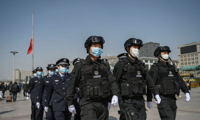 Los oficiales de policía chinos llevan máscaras protectoras mientras marchan en formación alejándose de la bandera nacional a media asta después de observar tres minutos de silencio para marcar el día nacional de luto por COVID-19 en la estación de ferrocarril de Beijing el 4 de abril de 2020. (Kevin Frayer/Getty Images)