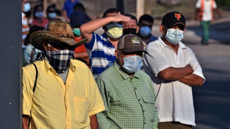 La gente lleva máscaras contra la propagación del virus del PCCh mientras hace cola en una calle de Tegucigalpa (Honduras), el 6 de abril de 2020. (ORLANDO SIERRA/AFP vía Getty Images)