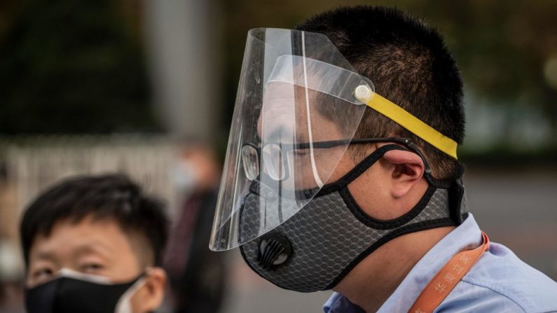 Un hombre (der.) con una máscara facial y un protector facial sale a la calle durante la hora pico en Beijing el 7 de abril de 2020. (Nicolas Asfouri / AFP/ Getty Images)
