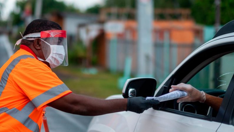 Un empleado municipal da literatura sobre el virus del PCCh a un automovilista en un punto de control en Loiza, Puerto Rico, el 7 de abril de 2020. (RICARDO ARDUENGO/AFP vía Getty Images)