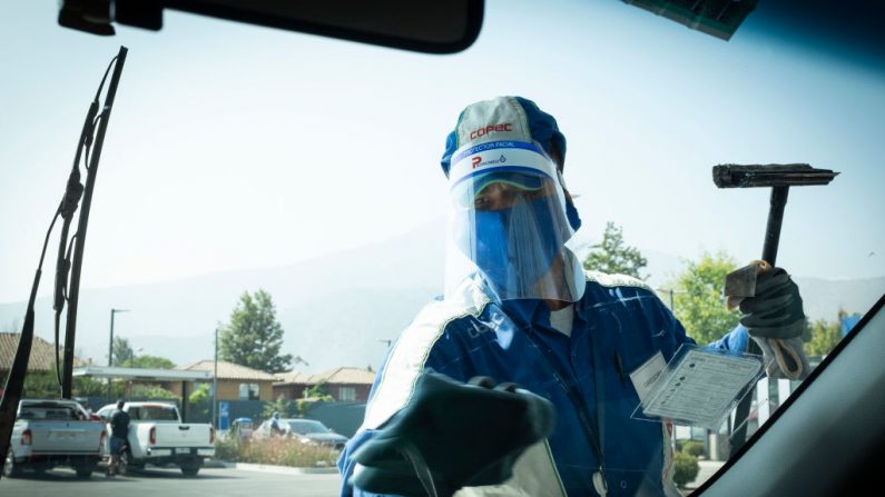 Un trabajador de una gasolinera usa guantes y una máscara facial como protección contra el virus del PCCh mientras limpia un parabrisas en Santiago, Chile, el 10 de abril de 2020. (MARTIN BERNETTI/AFP vía Getty Images)