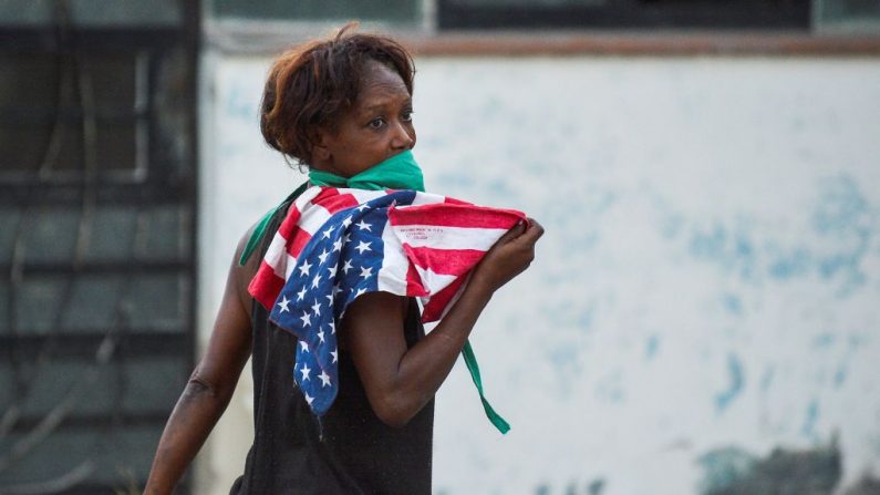 Una mujer con una máscara facial sostiene una bandera de EE.UU. mientras camina por una calle de La Habana, Cuba, el 13 de abril de 2020. (YAMIL LAGE/AFP vía Getty Images)