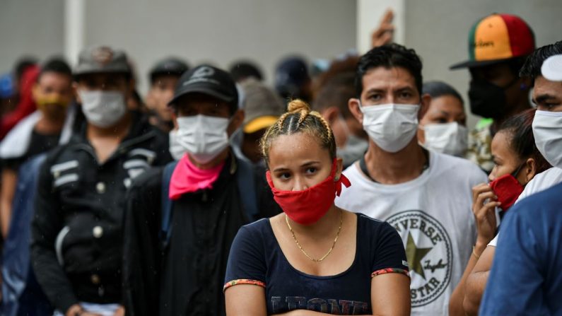 Migrantes venezolanos usan máscaras faciales mientras esperan ser revisados por trabajadores de la salud para descartar el virus del PCCh como parte de su proceso de repatriación en Cali, Colombia, el 13 de abril de 2020. (LUIS ROBAYO/AFP vía Getty Images)