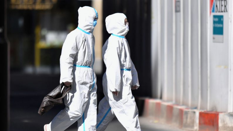 Una pareja lleva trajes protectores mientras camina por Market Street en el centro de la ciudad casi desierta de Manchester, al noroeste de Inglaterra, el 15 de abril de 2020, durante el encierro nacional para combatir el virus del PCCh. (ANTHONY DEVLIN/AFP vía Getty Images)