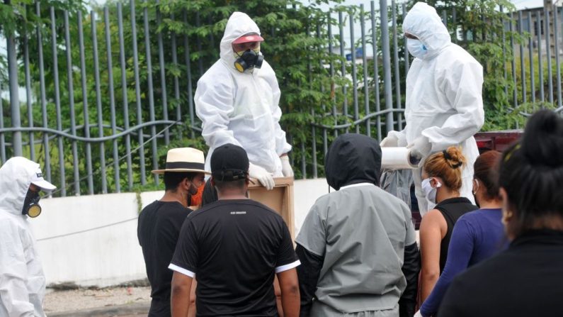 Trabajadores vestidos con trajes protectores envuelven con plástico un ataúd con los restos de una persona que murió por COVID-19, en las afueras de la morgue del Hospital General Guasmo Sur en Guayaquil, Ecuador, el 15 de abril de 2020. (JOSE SANCHEZ/AFP vía Getty Images)