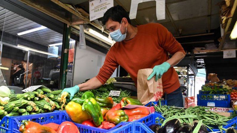 Un vendedor con mascarilla y guantes de protección atiende a un cliente en un puesto de frutas y verduras en el mercado local del distrito de Trionfale, en Roma, el 16 de abril de 2020. (ANDREAS SOLARO/AFP vía Getty Images)
