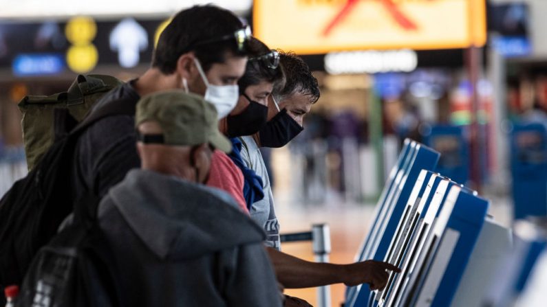 Los pasajeros llevan máscaras faciales mientras imprimen su tarjeta de embarque en el Aeropuerto Internacional de Santiago, en Santiago (Chile), el 20 de abril de 2020 durante la nueva pandemia de COVID-19. (MARTIN BERNETTI/AFP vía Getty Images)