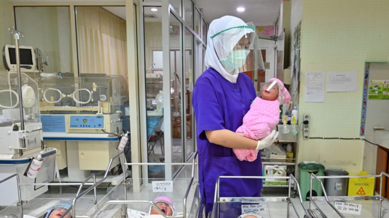  Una enfermera sostiene a un bebé recién nacido, visto usando una careta como medida de protección en medio de la pandemia del COVID-19, en un centro de maternidad el 21 de abril de 2020. (Foto de ADEK BERRY/AFP vía Getty Images)
