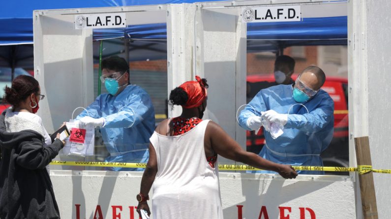 Miembros del Departamento de Bomberos de Los Ángeles realizan pruebas de COVID-19 a mujeres que llevan equipo de protección personal (PPE) en Skid Row en medio de la pandemia de coronavirus del 21 de abril de 2020 en Los Ángeles, California.(Mario Tama/Getty Images)